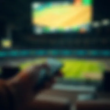 A hand holding a remote control while watching sports.